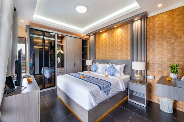 Modern Balinese bedroom interior with king-sized bed, wooden wall panels, mirrored wardrobe, and ambient lighting. - Bali Villas